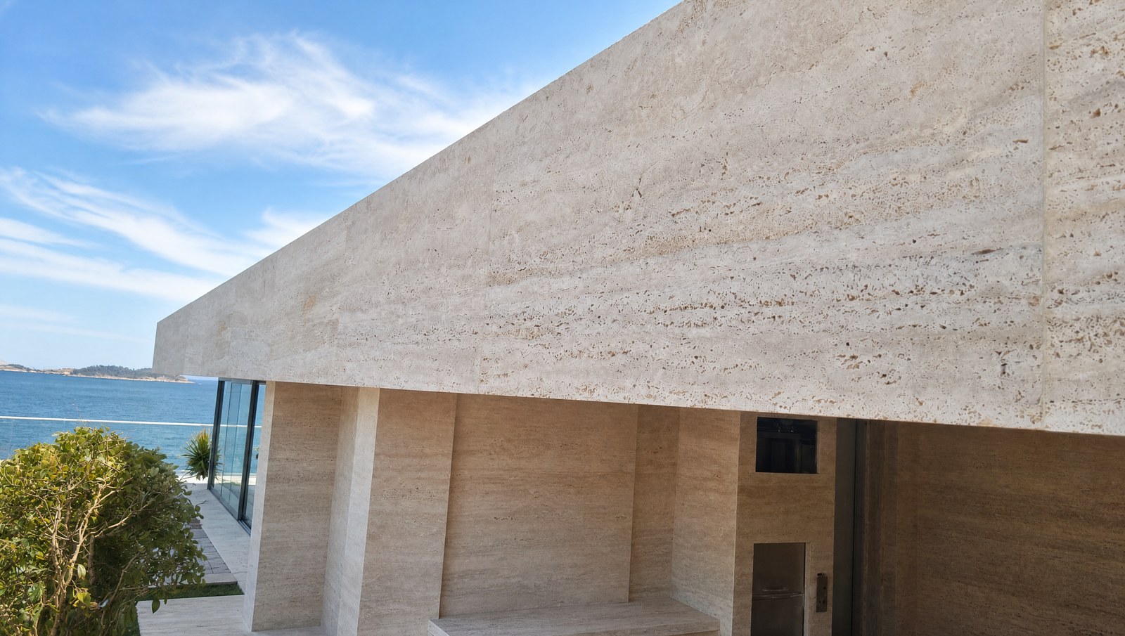 Fachada externa revestida em placa serrada de travertino, de superfície plana e junta fina