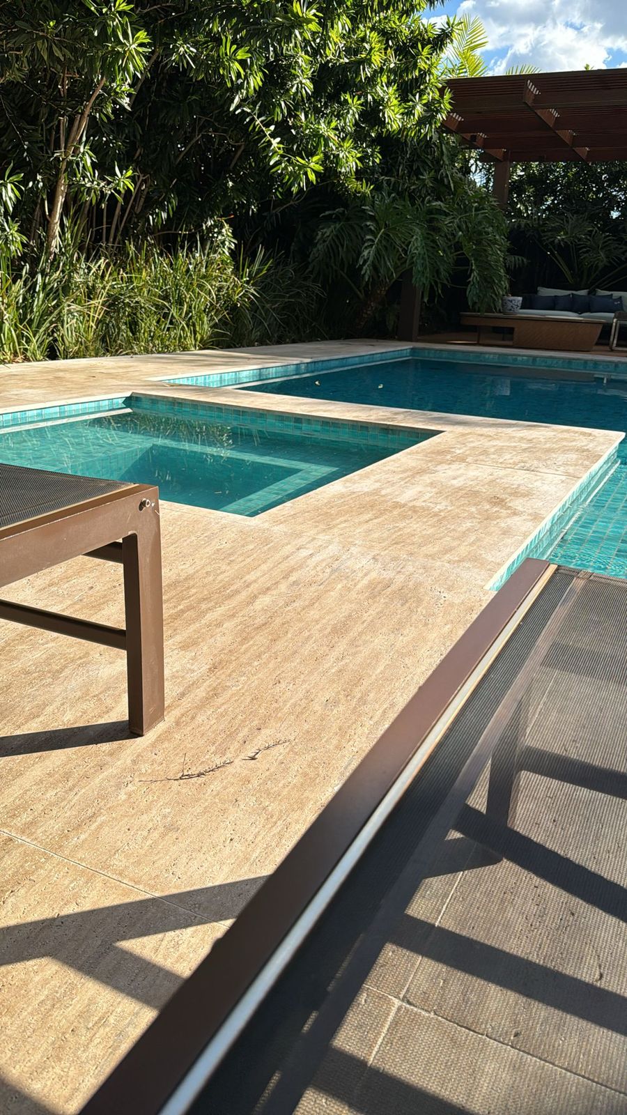 Deck de piscina em travertino romano DZ sob sol forte, com sombra de árvore sobre a pedra