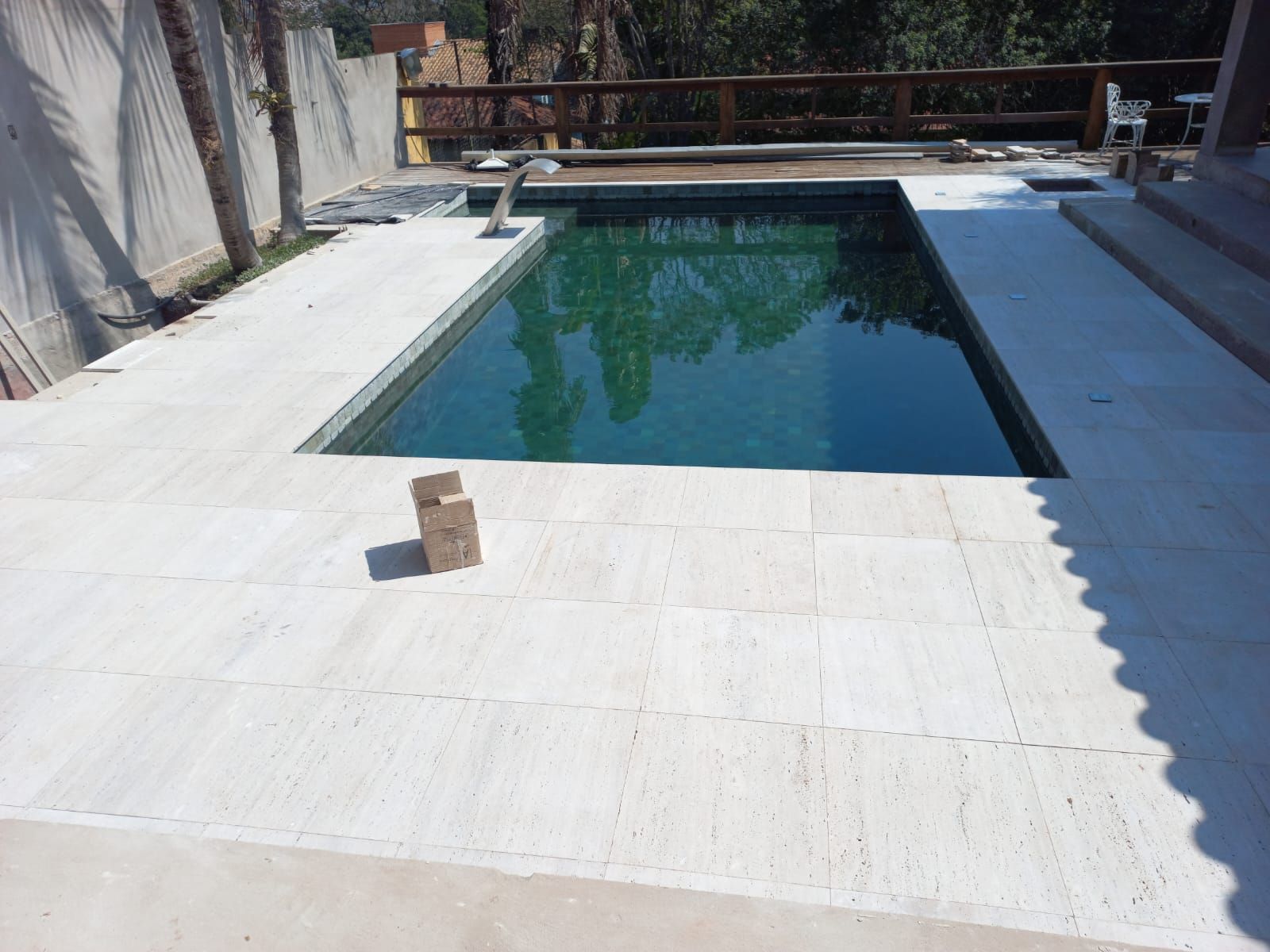 Deck claro de travertino romano contornando uma piscina, com área de estar externa ao lado