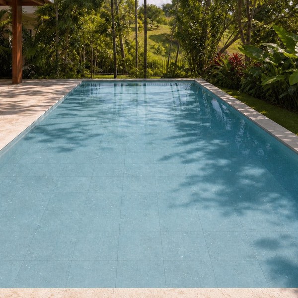 Piscina revestida em Pedra Aquamarine com a água em azul claro, cercada por vegetação tropical