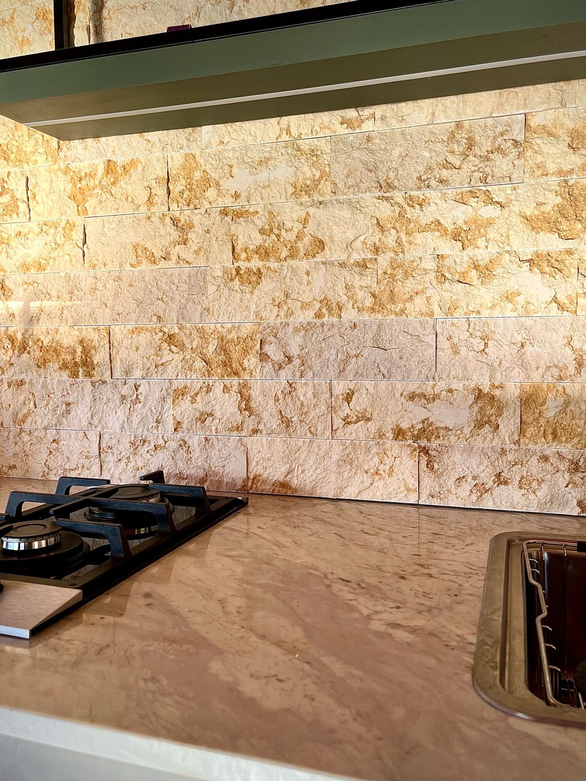Parede de Rock Face Cairo em fiadas corridas atrás de bancada de cozinha, sob luz quente rasante
