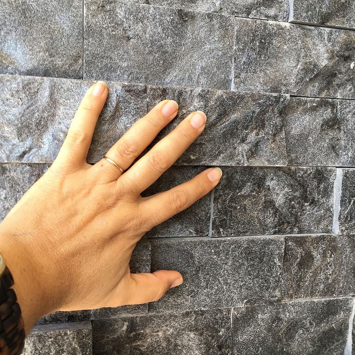 Mão apoiada em parede de Rock Face Matrix, dando a escala real da peça de 30x10 cm e a profundidade do relevo
