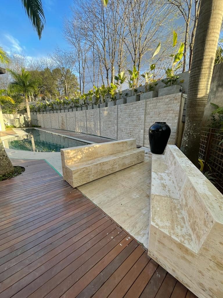 Muro comprido em rock face de travertino ao lado de piscina de raia e deck de madeira