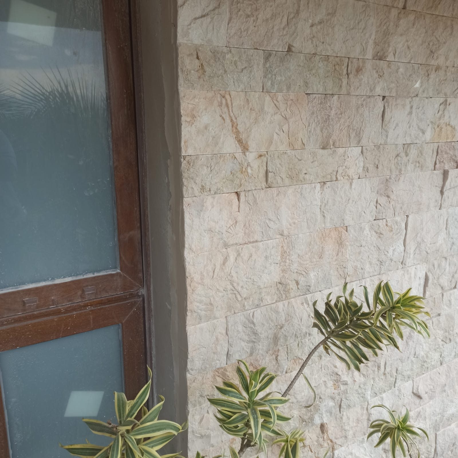 Parede externa em rock face de travertino, com a face bruta da rocha preservada e sombra entre as fiadas