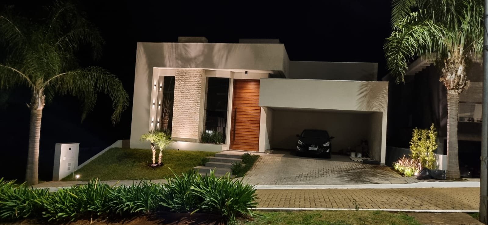 Fachada de casa com painel de rock face iluminado por luz rasante à noite