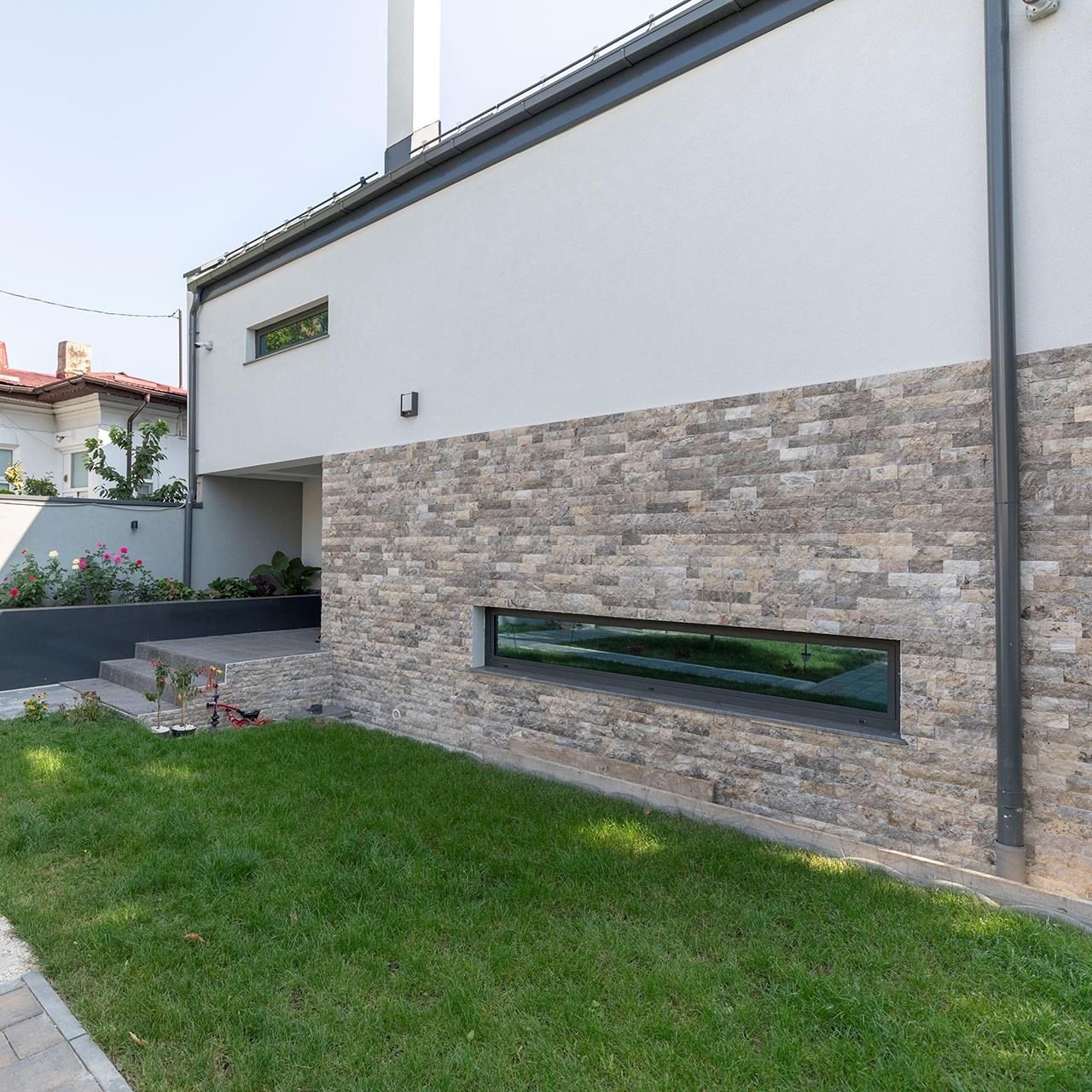 Fachada com faixa de embasamento revestida em Rock Face Travertino Silver, sob volume branco