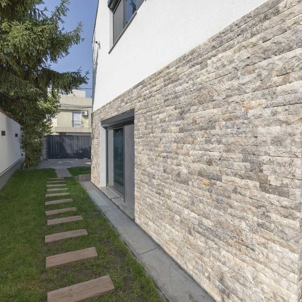 Parede externa de casa revestida em pedra natural cinza de relevo, ao longo de um jardim