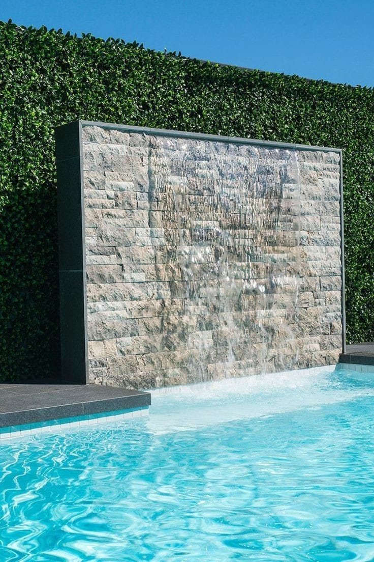 Muro em Rock Face Travertino Silver entre cerca viva e piscina, com lâmina d'água
