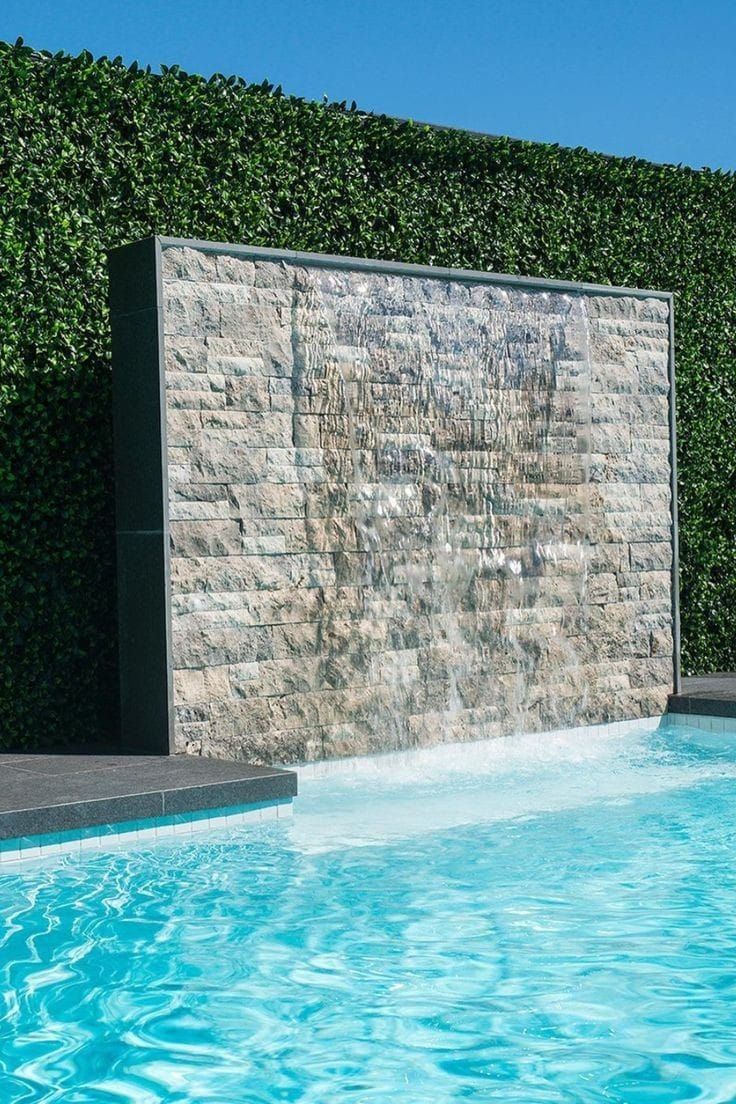 Parede externa em rock face de travertino silver ao lado de uma piscina, com o relevo criando sombra sob luz rasante