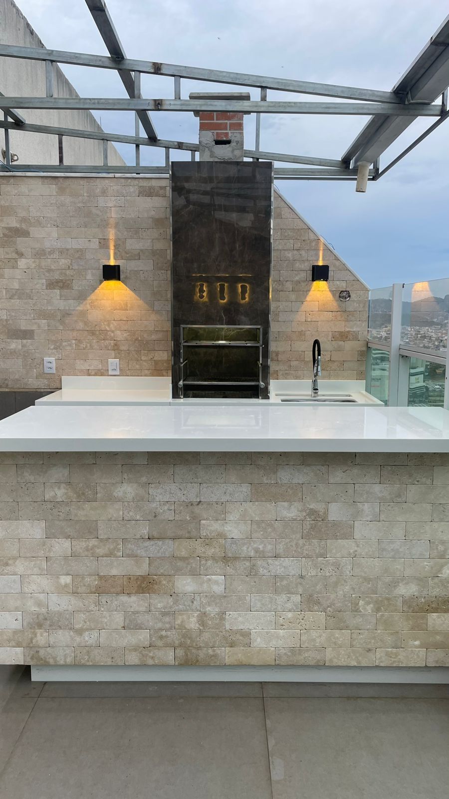 Área gourmet ao ar livre com parede e ilha revestidas em tijolinho de travertino anticato