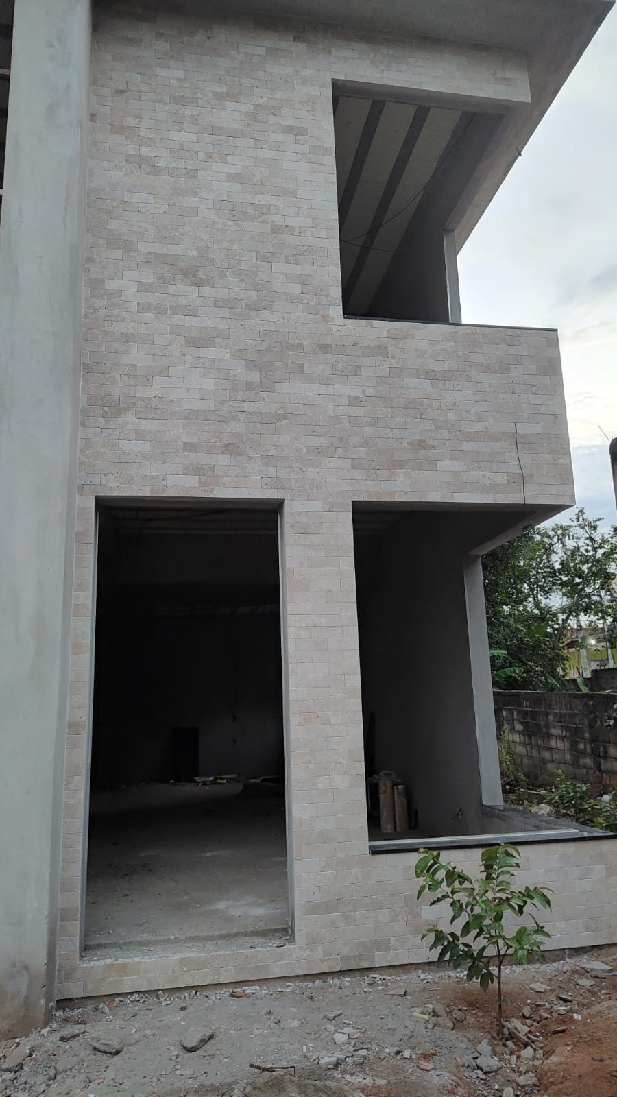 Fachada de dois pavimentos revestida em tijolinho de travertino anticato, com a obra ainda em execução