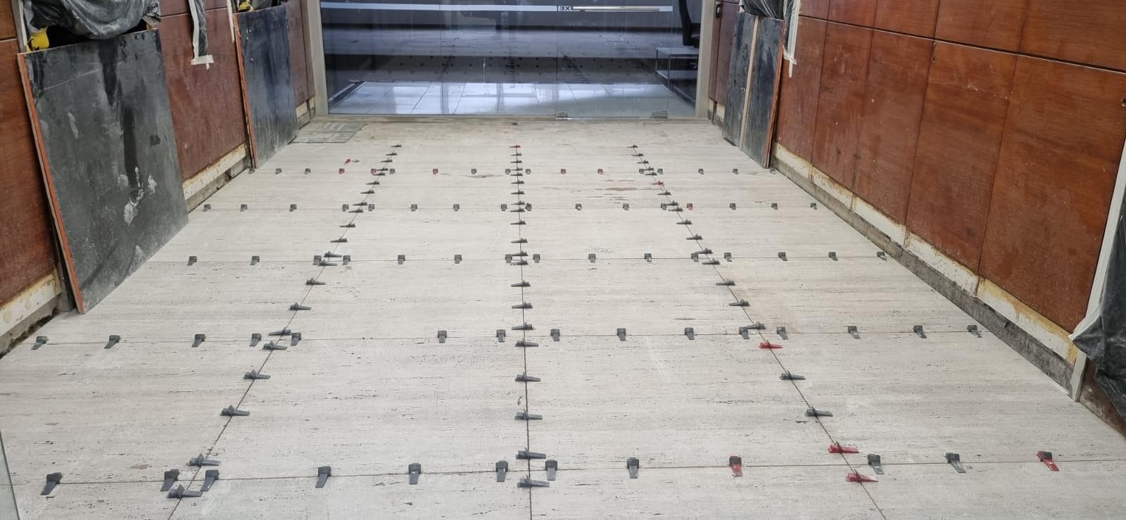 Piso de travertino romano recém assentado em obra, com espaçadores niveladores marcando as juntas de toda a paginação