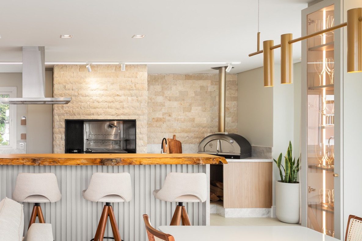 Área gourmet com churrasqueira e forno de pizza em parede de rock face travertino claro