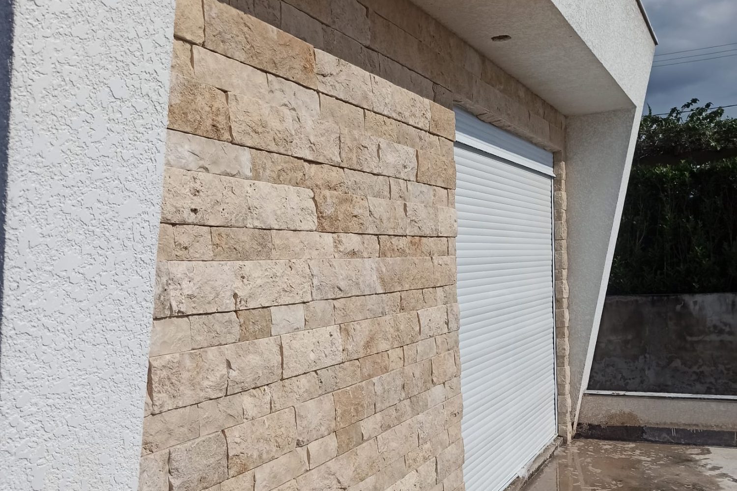 Parede externa em rock face travertino claro sob luz rasante