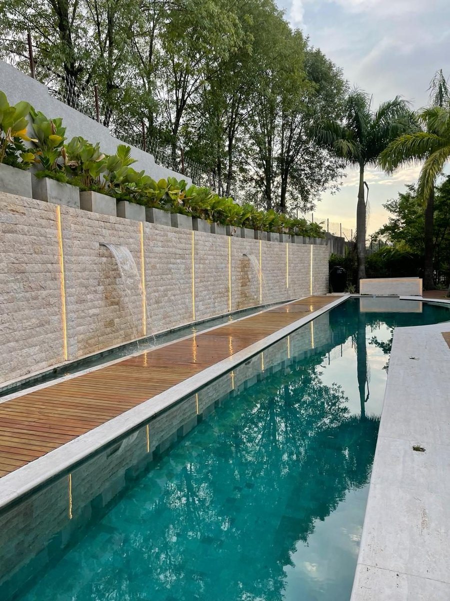 Muro externo revestido com pedra travertino rockface ao lado da piscina